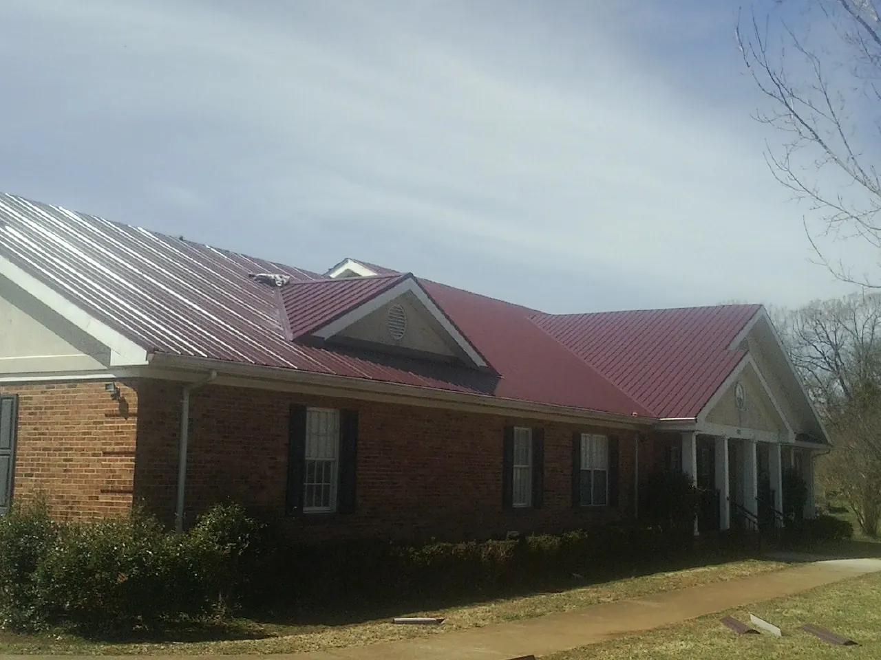 Red metal roof with gabled entries on a long brick building, from a Hail Damage Roof Repair job in Silverado