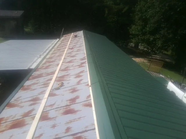Old rusted panels beside newly installed green metal roofing — Wind Damage Roof Repair by Roofing Brothers in Silverado