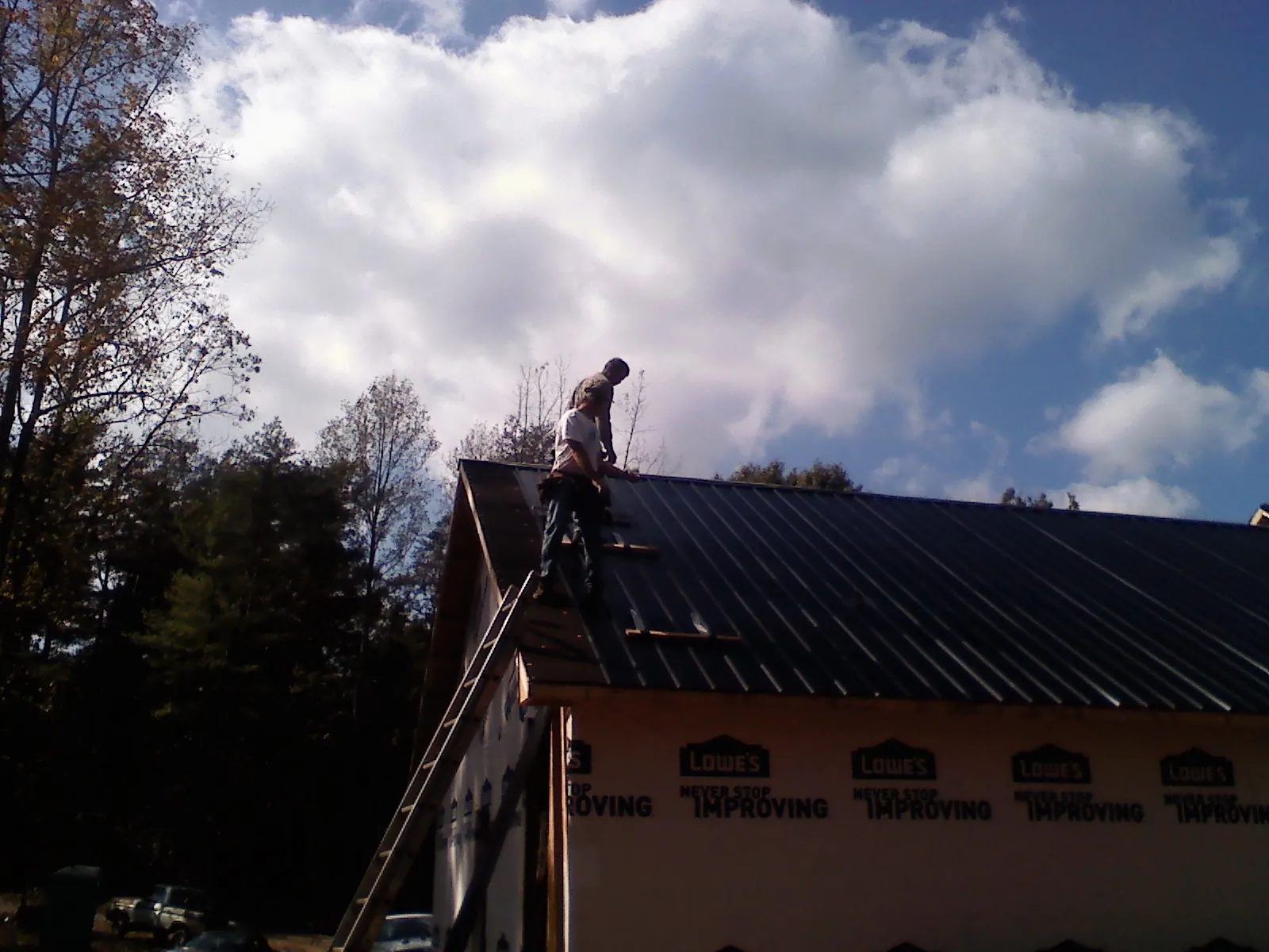 Roofer fastening dark metal panels high against a cloudy sky, from a Roof Inspection job in Silverado