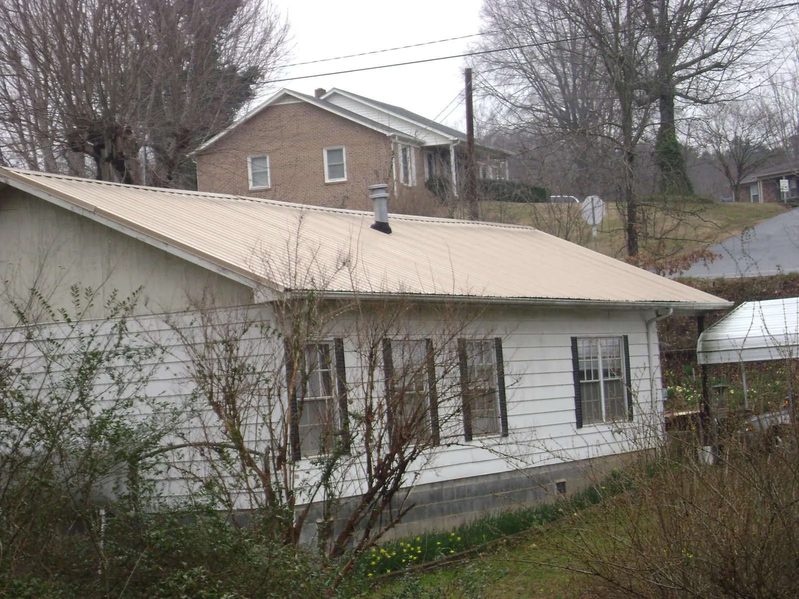 Tan metal roof on a white sided house set into a hillside — Commercial Roofing by Roofing Brothers in Silverado